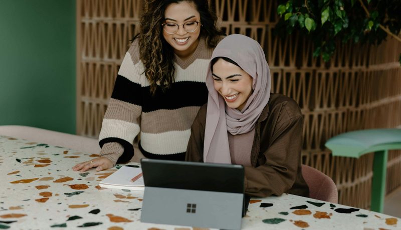 Two women sitting at a table with a laptop